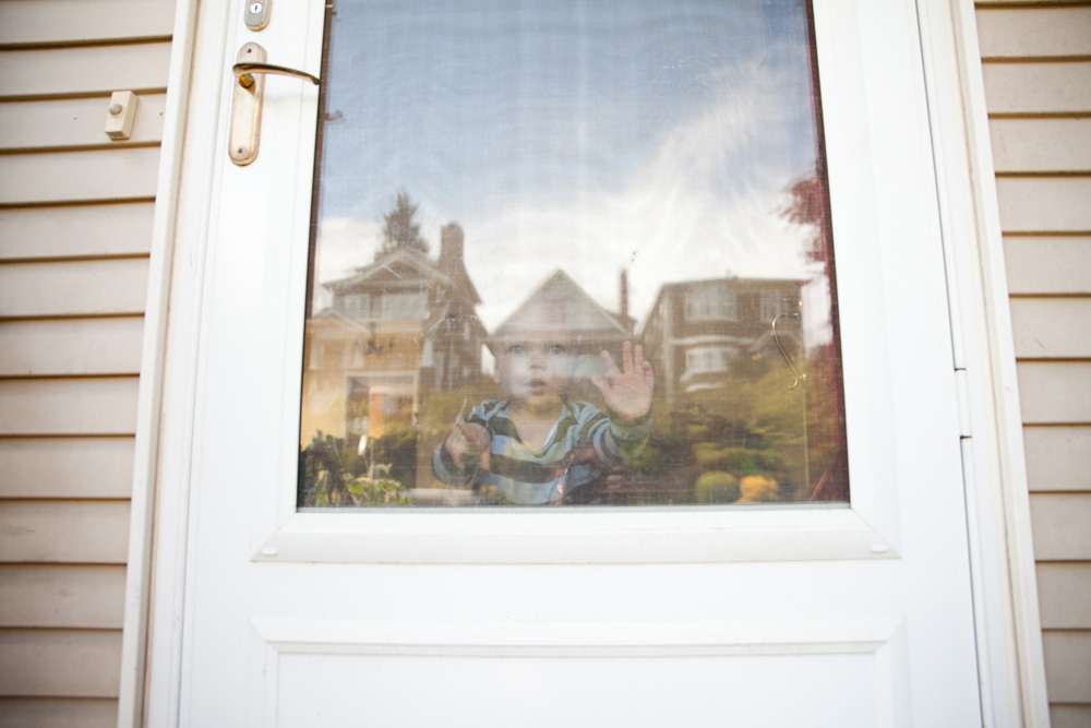 documentary family photography - baby looking through the window with reflection